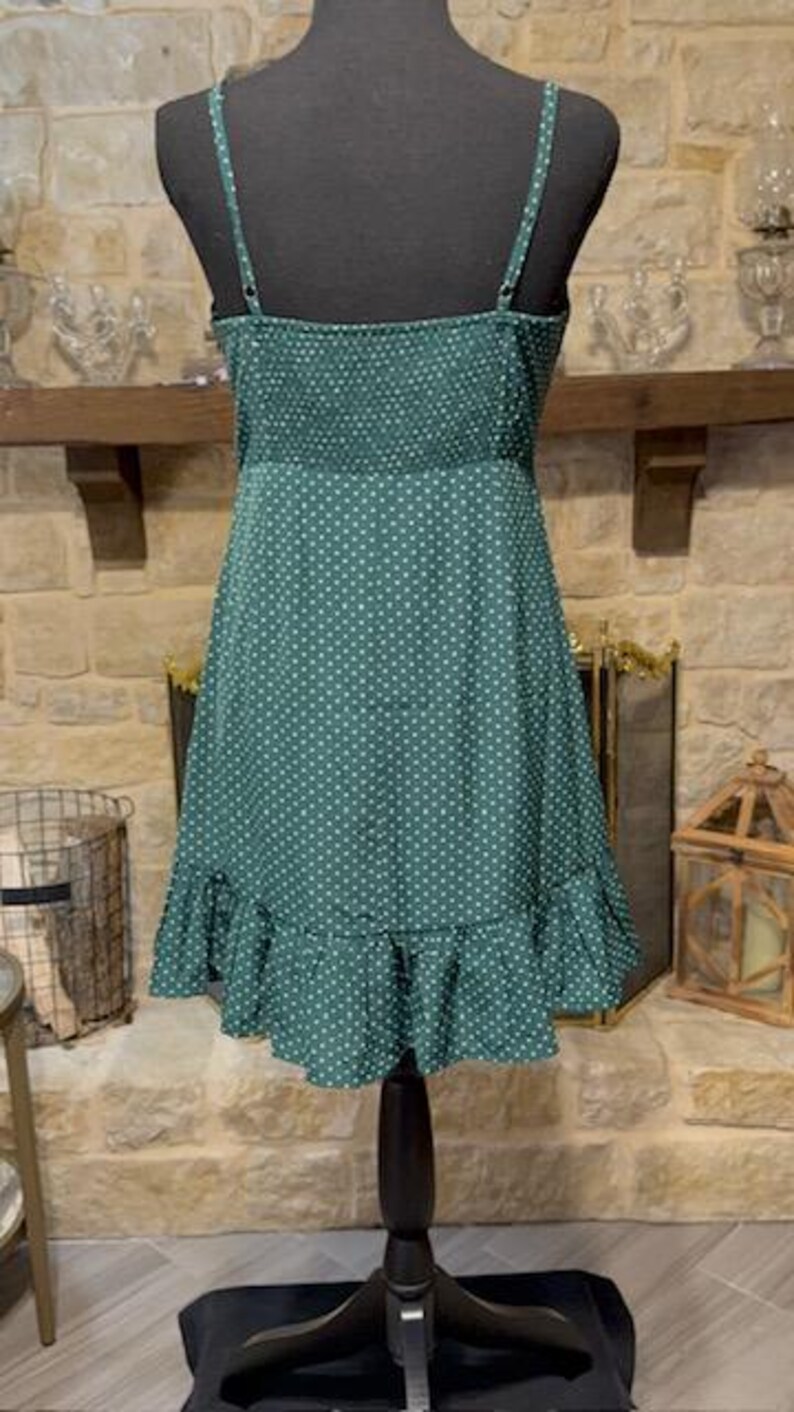 May include: A green polka dot dress with a ruffled hem. The dress has thin straps and a fitted bodice.