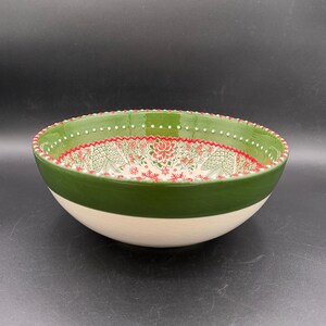 May include: A ceramic bowl with a green rim and a white base. The interior features a red and green floral pattern. The bowl's rim has a dotted design. This decorative bowl is suitable for serving food.