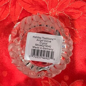 Puede incluir: Un portavelas de vidrio transparente con un dise&ntilde;o texturizado. La etiqueta dice "Holiday Traditions&trade; Angel Votive Crystal SKU#6215040 Made in Germany".