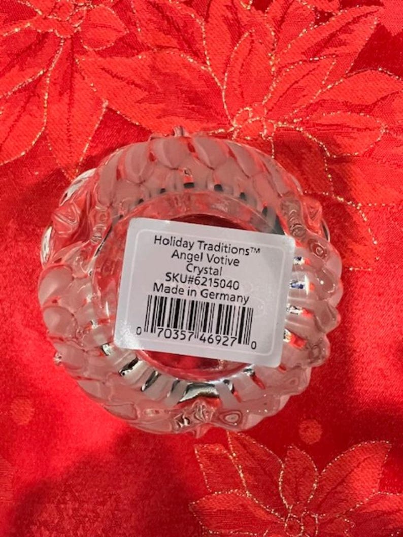 Puede incluir: Un portavelas de vidrio transparente con un dise&ntilde;o texturizado. La etiqueta dice "Holiday Traditions&trade; Angel Votive Crystal SKU#6215040 Made in Germany".