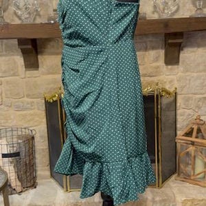 May include: A green polka dot dress with a ruffled hem. The dress is sleeveless and has a fitted bodice. The dress is on a mannequin.
