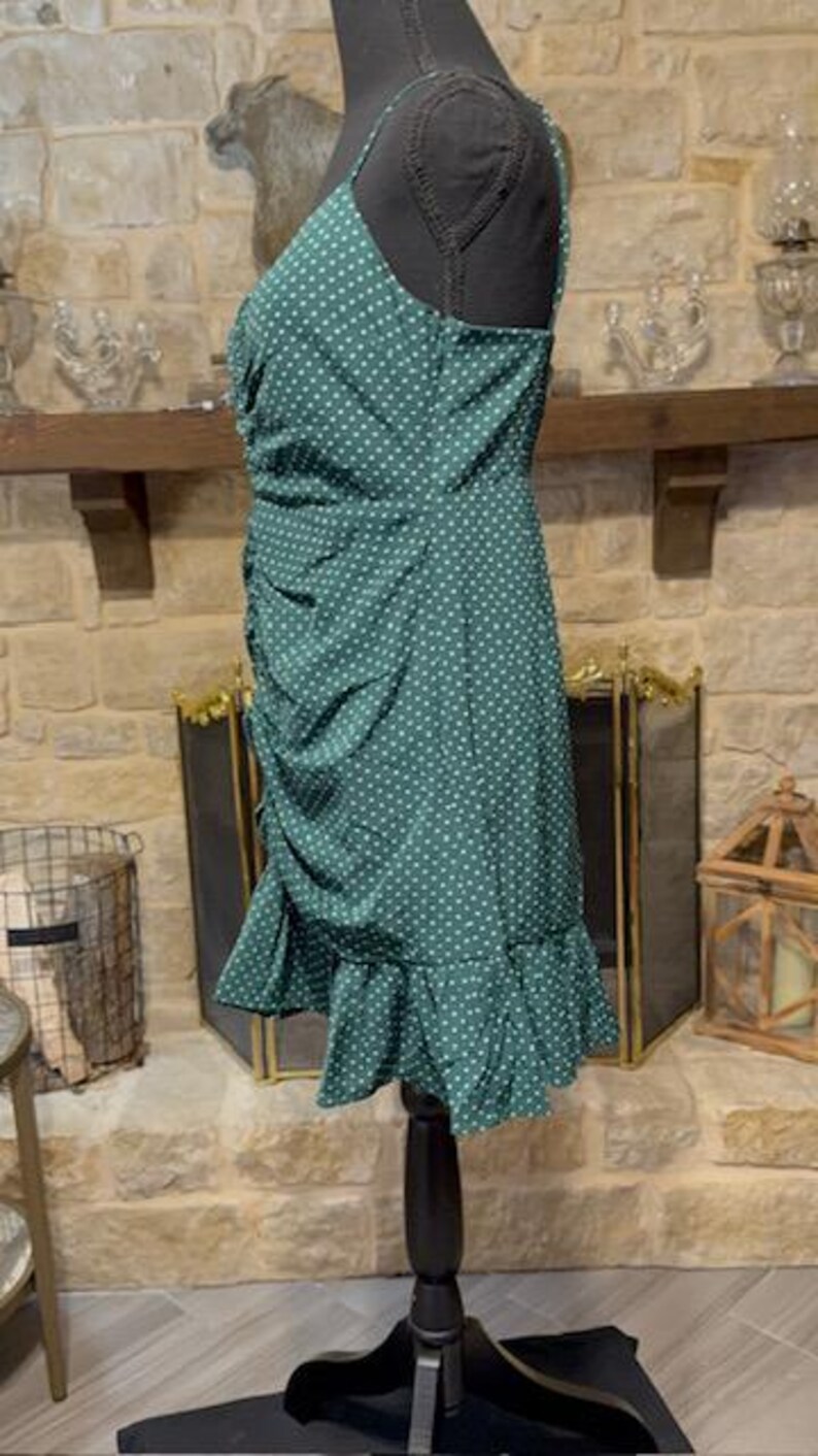 May include: A green polka dot dress with a ruffled hem. The dress is sleeveless and has a fitted bodice. The dress is on a mannequin.
