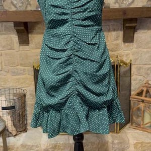May include: A green polka dot dress with a ruffled hem. The dress has a fitted bodice and a loose, flowing skirt.