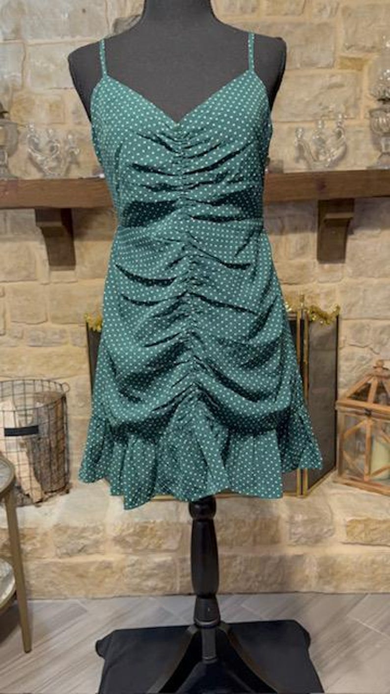 May include: A green polka dot dress with a ruffled hem. The dress has a fitted bodice and a loose, flowing skirt.