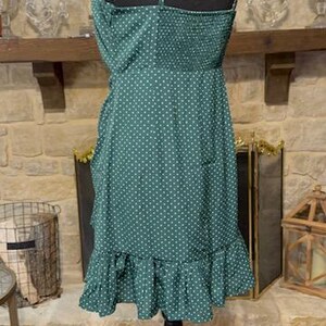 May include: A green and white polka dot dress with a ruffled hem and adjustable straps. The dress is on a mannequin and is photographed from the back.