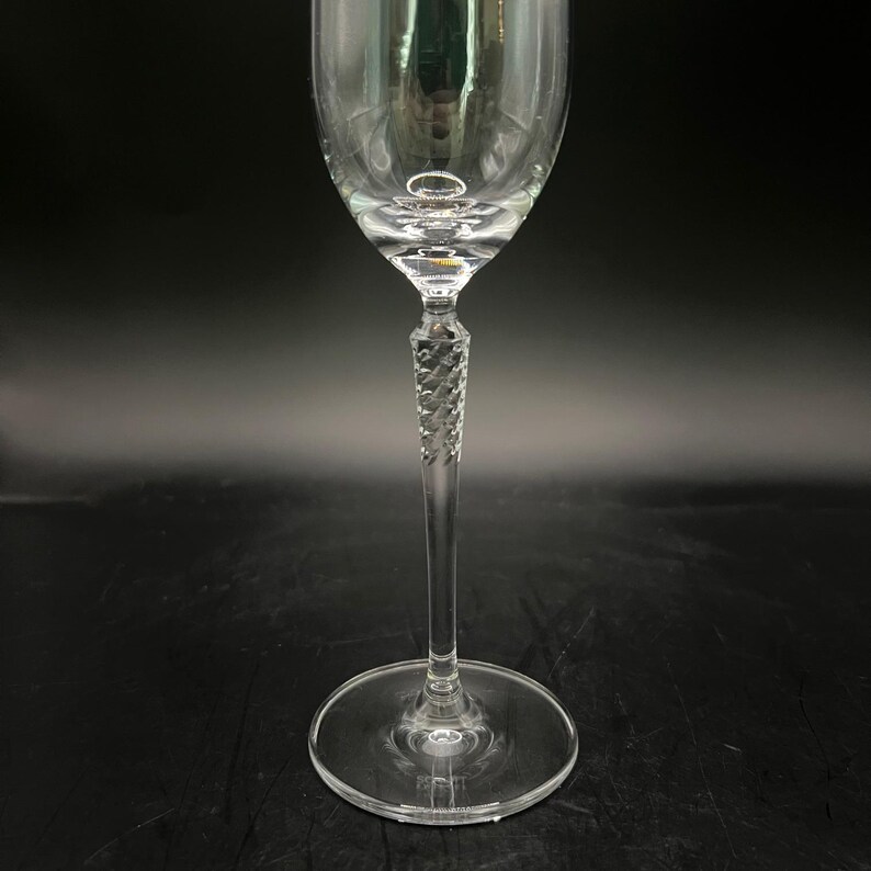 May include: A clear wine glass with a twisted stem and a circular base. The glass is designed for serving wine. The stem has a decorative, twisted design. The glass is made of clear glass and reflects light.