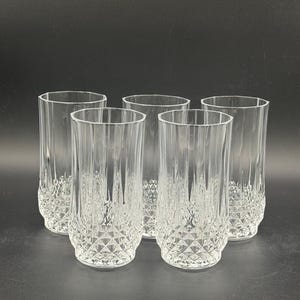May include: A set of five clear glass tumblers featuring a vertical ribbed pattern on the upper portion and a textured diamond-cut design around the base. Each tall drinking glass has a cylindrical shape with a smooth rim and a heavy, clear base.