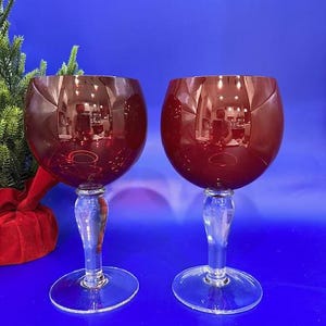 Puede incluir: Dos copas de vino tinto con tallos y bases transparentes. Las copas son de vidrio y tienen un color rojo intenso.