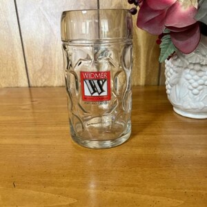 Puede incluir: Un jarro de cerveza de vidrio transparente con una superficie texturizada. El jarro tiene un logotipo en la parte delantera que dice "Widmer Brewing Company, Portland, Oregon".