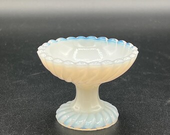 Può includere: Una piccola e ornata coppetta in vetro con piedistallo e bordo smerlato. La coppetta presenta una combinazione di colori bianco e pesca chiaro con un design a torsione sulla coppa e sulla base. Il bordo e la base hanno un accento azzurro.