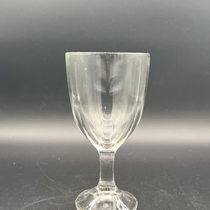 May include: A clear, stemmed glass with a rounded bowl and a textured, vertical ribbed design. The glass has a short stem and a circular base. The glass is empty and appears to be made of glass.