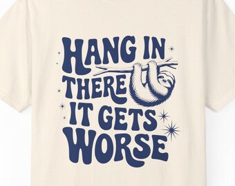 May include: A cream-colored t-shirt with a blue graphic of a sloth hanging from a branch. The graphic says "Hang in there it gets worse".