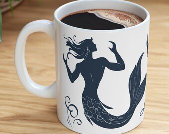 May include: White ceramic mug with a black silhouette of a mermaid with a tail and long hair. The mug is filled with coffee.