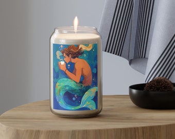 May include: A white candle with a blue and green illustration of a mermaid holding a cup. The mermaid has brown hair and is surrounded by bubbles.