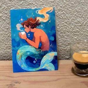 A colorful illustration of a merman drinking from a white cup. He has wavy brown hair, and a shimmering teal and green tail. The overall style is whimsical and dreamy, with a warm color palette contrasting against the cool blue tones of the water.