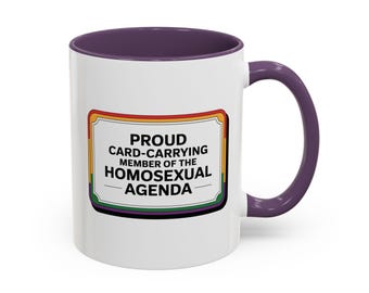 May include: White ceramic coffee mug with a purple rim and handle. The mug features a graphic of a rainbow-colored sign that reads "Proud Card-Carrying Member of the Homosexual Agenda."