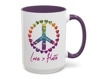 May include: White ceramic coffee mug with a purple rim and handle. The mug features a rainbow peace sign surrounded by hearts and the text "Love > Hate" in pink.