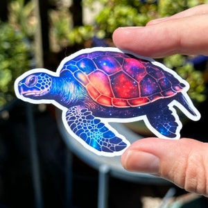 May include: A colorful sticker of a sea turtle with a galaxy design. The turtle's shell is a mix of red, orange, blue, and purple, with a starry pattern. The sticker is perfect for adding a touch of whimsy to laptops, water bottles, or journals.