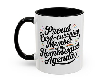 May include: White ceramic coffee mug with a black rim and handle. The mug features a black graphic that says "Proud Card-carrying Member of the Homosexual Agenda" with a rainbow stripe.