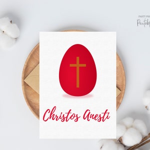 May include: Printable Easter card featuring a red egg with a gold cross. The text "Christos Anesti" is written in red cursive.