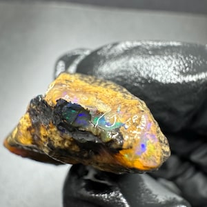 May include: A rough, dark brown and orange opal with a flash of iridescent green, blue, and purple.