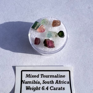 May include: A small collection of mixed tourmaline gemstones from Namibia, South Africa. The gemstones are various shades of pink, green, and blue. The total weight of the gemstones is 6.4 carats.  Mixed Tourmaline Namibia, South Africa Weight 6.4 Carats