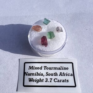 May include: A small container of mixed tourmaline gemstones from Namibia and South Africa, weighing 3.7 carats. The gemstones are pink, green, and brown.