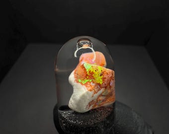 May include: A clear glass pendant with a white and orange opal stone inside. The stone has a green and yellow iridescent sheen.