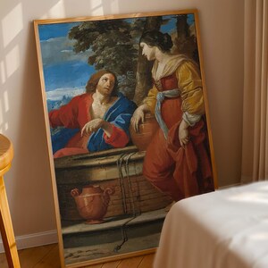 May include: A framed painting depicting a biblical scene. The artwork features two figures, one in red and blue robes, the other in a red and yellow dress. The background includes a blue sky, trees, and a well. The frame is made of wood.