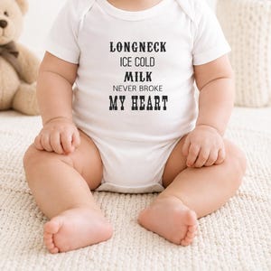 May include: A white baby onesie with the text "LONGNECK ICE COLD MILK NEVER BROKE MY HEART" in black. The baby is sitting on a cream-colored blanket.