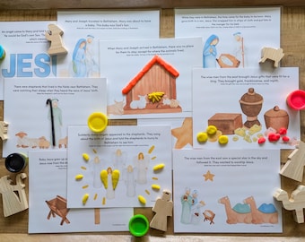 May include: Illustrated cards telling the Nativity story, with wooden figures of angels, sheep, and camels. The scenes are accented with colourful playdough, and the word "JESUS" is written in blue.