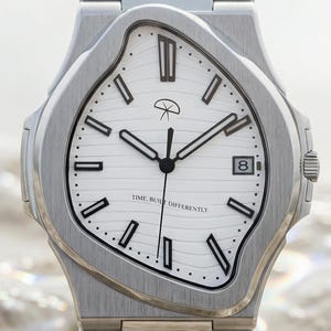 Puede incluir: Un reloj de pulsera de acero inoxidable con una esfera blanca única de estilo derretido. El reloj presenta manecillas negras, una ventana de fecha y el texto "TIME RUNS DIFFERENTLY". La correa del reloj también es de acero inoxidable.