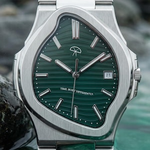 Puede incluir: Un reloj de pulsera de acero inoxidable con esfera verde y visualización de fecha. El reloj tiene un diseño de bisel ondulado único y una correa de acero inoxidable a juego. La esfera del reloj presenta un logotipo y el texto "TIME BUILT DIFFERENTLY".