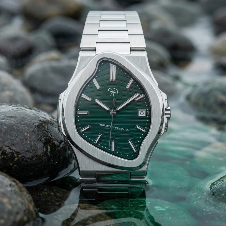 May include: A silver wristwatch with a green face and a date display. The watch has a distinctive, wavy bezel design and a matching silver strap. The watch face features a logo and the text "TIME BUILT DIFFERENTLY".