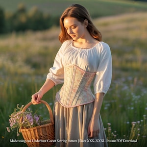 May include: A floral underbust corset with pink trim is worn over a white blouse and a long skirt. The corset features a delicate floral pattern. A basket of flowers is held in the foreground. The text reads: Made using our Underbust Corset Sewing Pattern | Sizes XXS-XXXL Instant PDF Download.