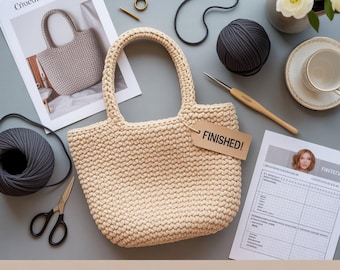 May include: A cream-coloured crochet handbag with a tag reading "FINISHED!" is the central object. The image also features grey yarn, scissors, a crochet hook, and a magazine showing a similar bag. The text at the bottom says "Make your own cute crochet handbag - easy PDF pattern."