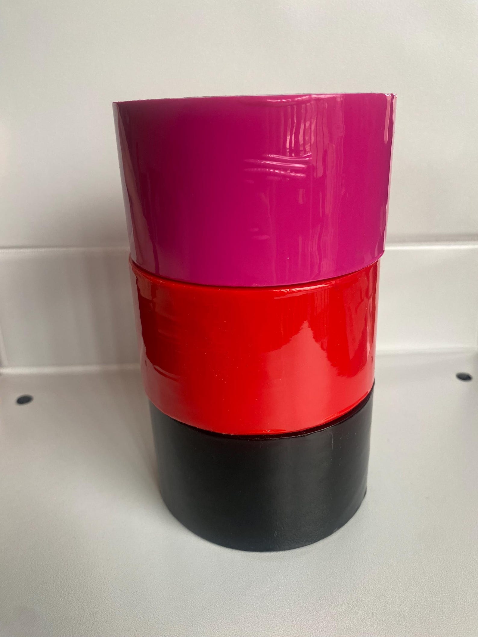 Close-up of static cohesive bondage tape rolls in red, pink, and black for restraint sex and bdsm bondage wear.