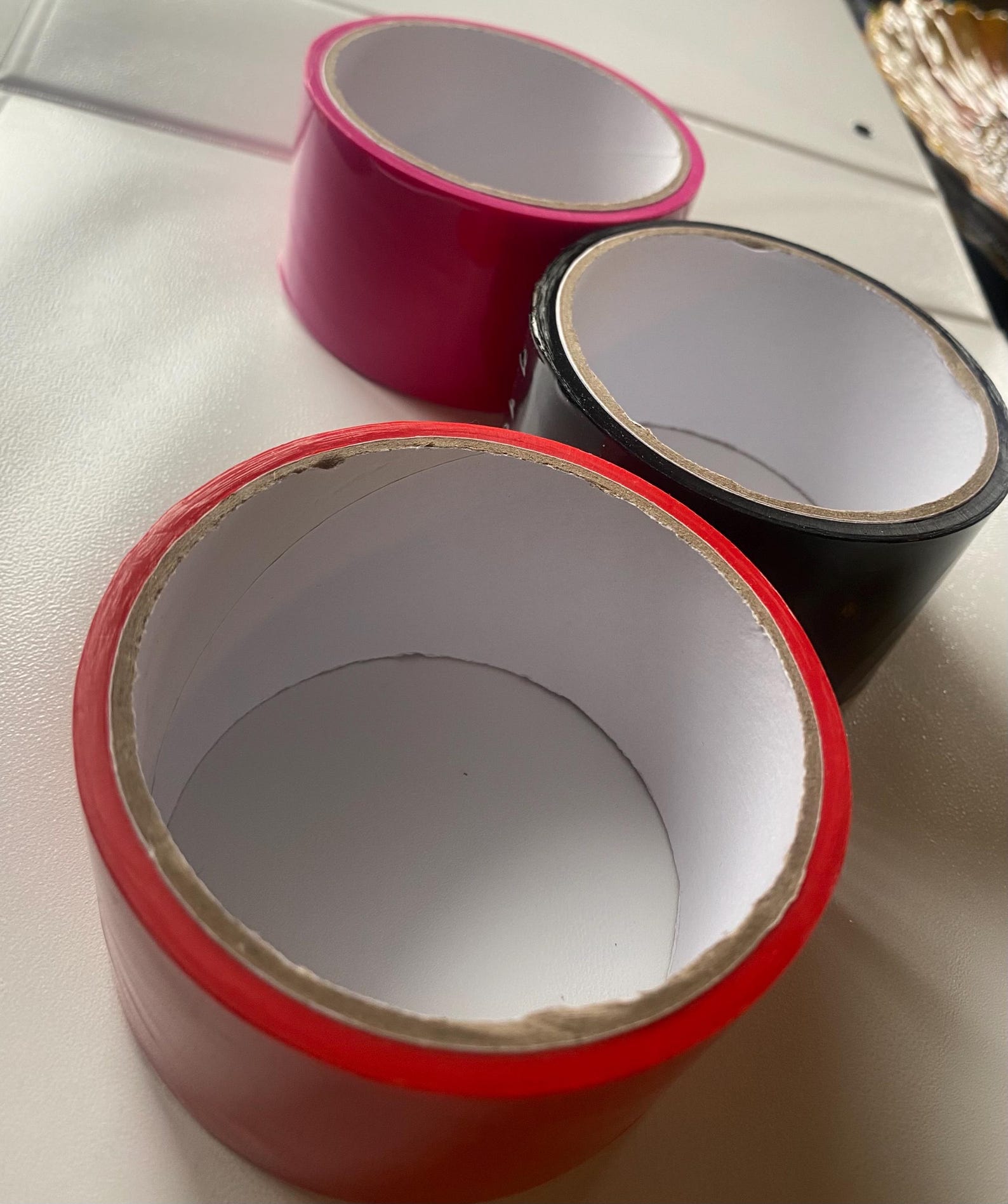 Rolls of red, pink, and black bondage tape stacked for bdsm ties, bondage restraints, and kinky handcuff bondage play.