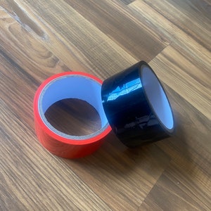 May include: Two rolls of tape, one red and one black, on a wood floor.