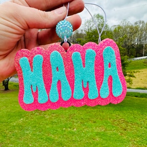 May include: Pink and blue glitter car air freshener with the word "MAMA" in large, blue, bubble letters.
