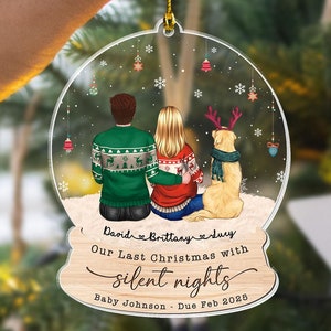 May include: A clear acrylic Christmas ornament with a snow globe design. It features a couple and a dog, with the text "Our Last Christmas with silent nights." The ornament is held by a gold string.