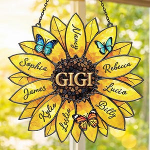 May include: A yellow sunflower-shaped stained glass window hanging with the name "GIGI" in the center. The sunflower petals have names like "Sophia" and "Nancy" written on them, with butterflies.