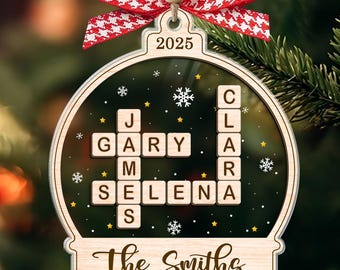 May include: Wooden Christmas ornament with a clear center, featuring names spelled out in Scrabble-style tiles. The ornament is topped with a red and white checkered bow and the year 2025. The bottom reads "The Smiths".