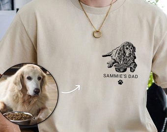 May include: A beige t-shirt with a black and white illustration of a dog eating from a bowl. The text "Sammie's Dad" is printed below the illustration.
