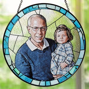 May include: A stained glass round hanging ornament with a blue and white border. The ornament features a portrait of a man and a young child. The man is wearing a blue shirt and the child is wearing a plaid dress.