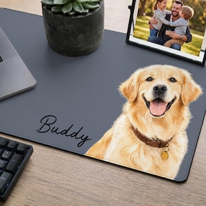 May include: A gray desk mat with a smiling golden retriever illustration and the name "Buddy" in script. A framed photo and a potted succulent sit on the mat. A laptop and keyboard are also visible.