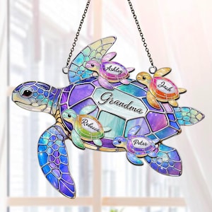 May include: A decorative, stained-glass style turtle ornament with the word "Grandma" and the names "Ashley", "Jack", "Rebecca", and "Peter". The turtle is primarily blue, purple, and green, with a black chain for hanging.