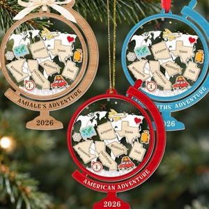 May include: Three globe-shaped ornaments in wood, blue, and red. Each features a world map, state outlines labeled Arizona, Texas, Minnesota, California, Missouri, and Utah, plus icons of a plane, car, and suitcase. Text includes 2026 and custom names.