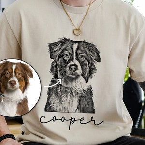 May include: Beige t-shirt featuring a black and white illustration of a dog's face, with the name "cooper" in cursive below. A smaller, color photo of the dog is in a circle on the left. The dog has brown and white fur.