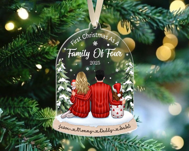 May include: A clear, bell-shaped acrylic Christmas ornament featuring an illustration of a family of four in red pajamas. The text reads First Christmas As A Family Of Four 2025, with the names Jason, Mommy, Daddy, and Isabel printed at the base.